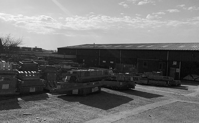Industrial yard with stacked metal materials and a warehouse under a partly cloudy sky.