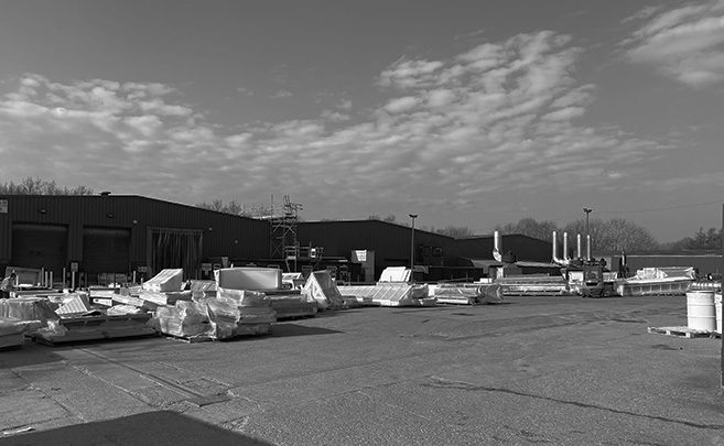 Outdoor industrial yard with stacked materials and warehouses under a partly cloudy sky.